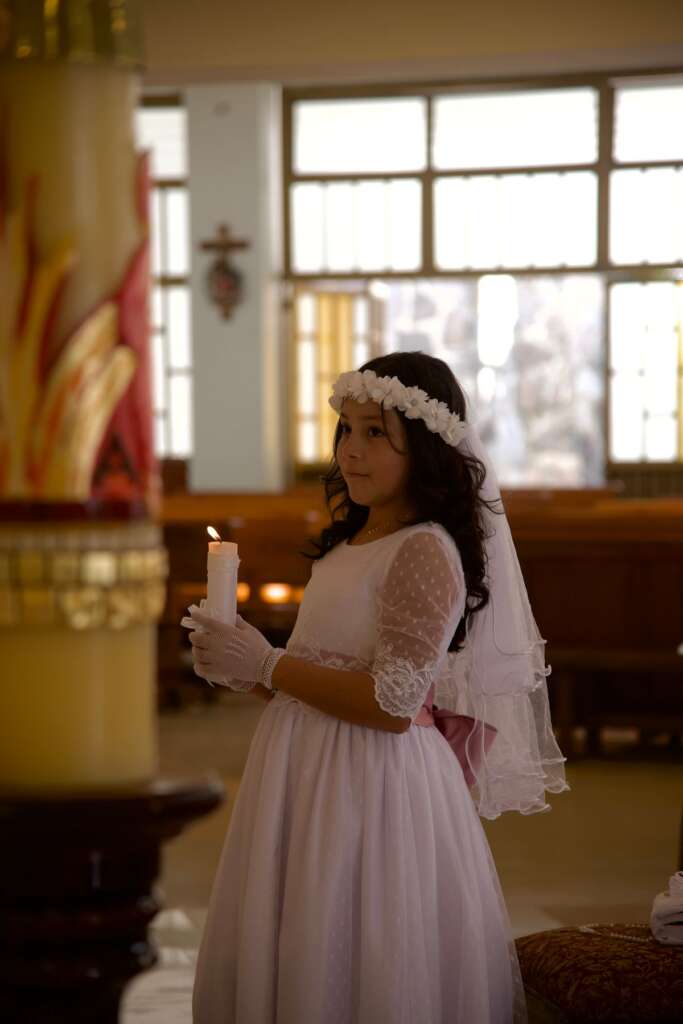 First communion girl holding her candle in church